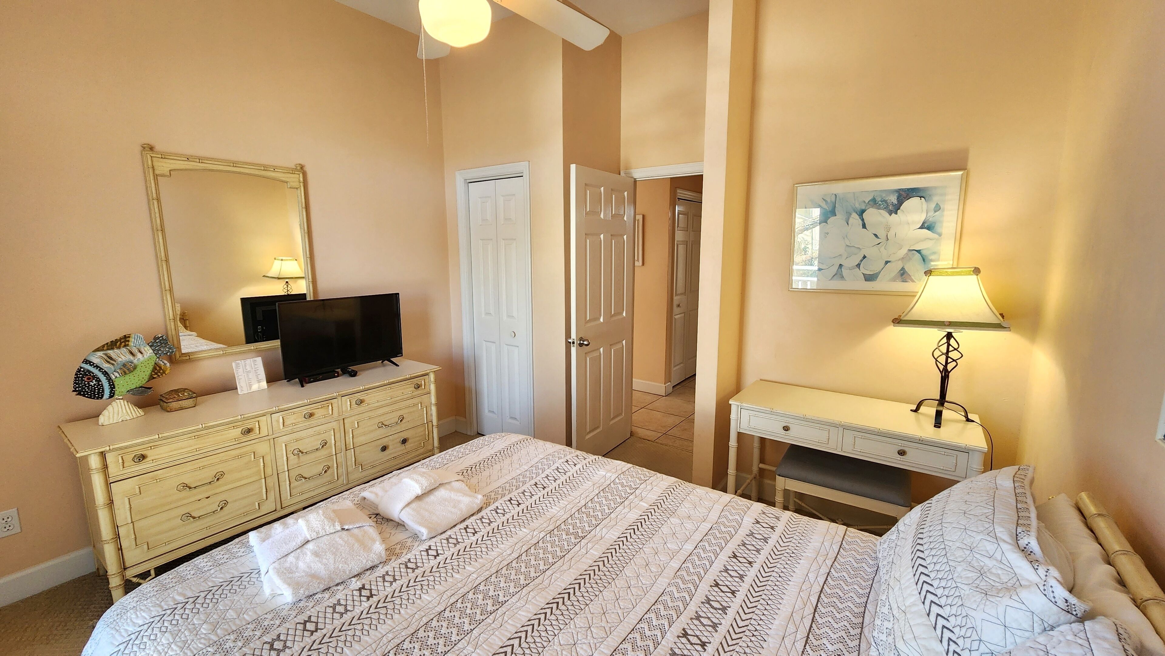 A bedroom with a bed, dresser, television, and a door leading to another room.