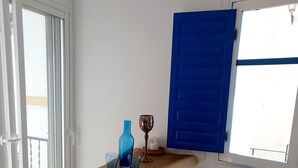 A small room with a wooden table, two stools, a blue door, and a window. - Mi Sueño Azul Torrox Pueblo (Torrox)