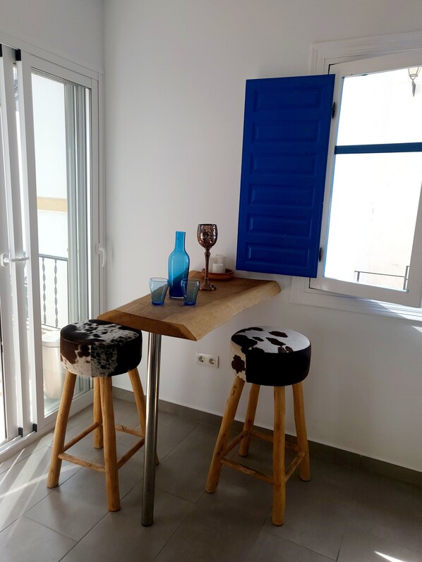 A small room with a wooden table, two stools, a blue door, and a window. - Mi Sueño Azul Torrox Pueblo (Torrox)