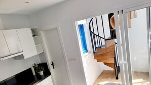 A modern kitchen with white cabinets, a black countertop, and a wooden dining table with plates and a glass. - Mi Sueño Azul Torrox Pueblo (Torrox)