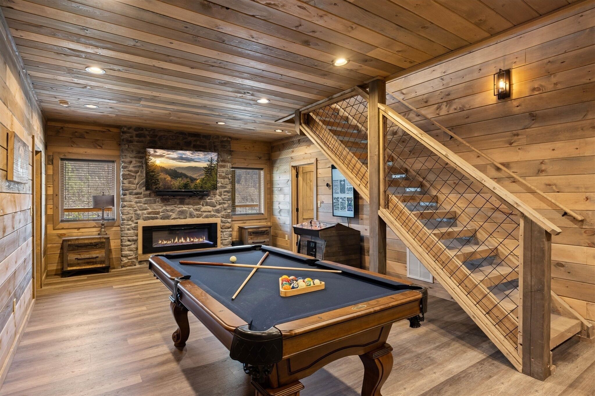 Interior de madera con mesa de billar, chimenea de piedra y una escalera.
