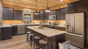 A modern kitchen with dark wood cabinets, stainless steel appliances, and a granite countertop. - Over The Top 5 Bedroom Cabin by RedAwning (Sevierville)