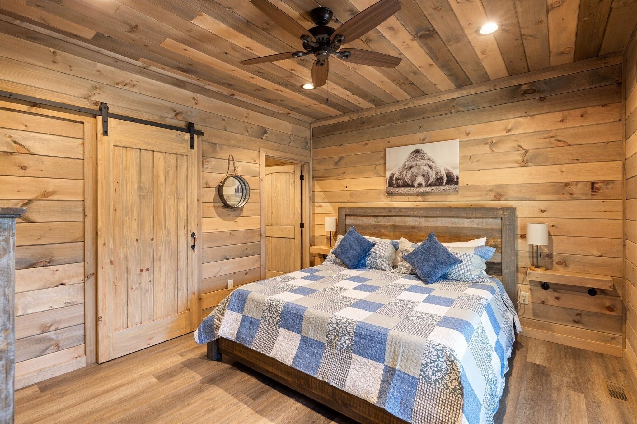 A bedroom with a wooden slat ceiling, a bed with a blue and white checkered bedspread, and a ceiling fan.