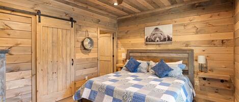 A bedroom with a wooden slat ceiling, a bed with a blue and white checkered bedspread, and a ceiling fan.