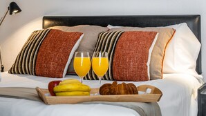 A neatly made bed with a tray of breakfast items, a modern abstract painting above it, and a lamp to the left.