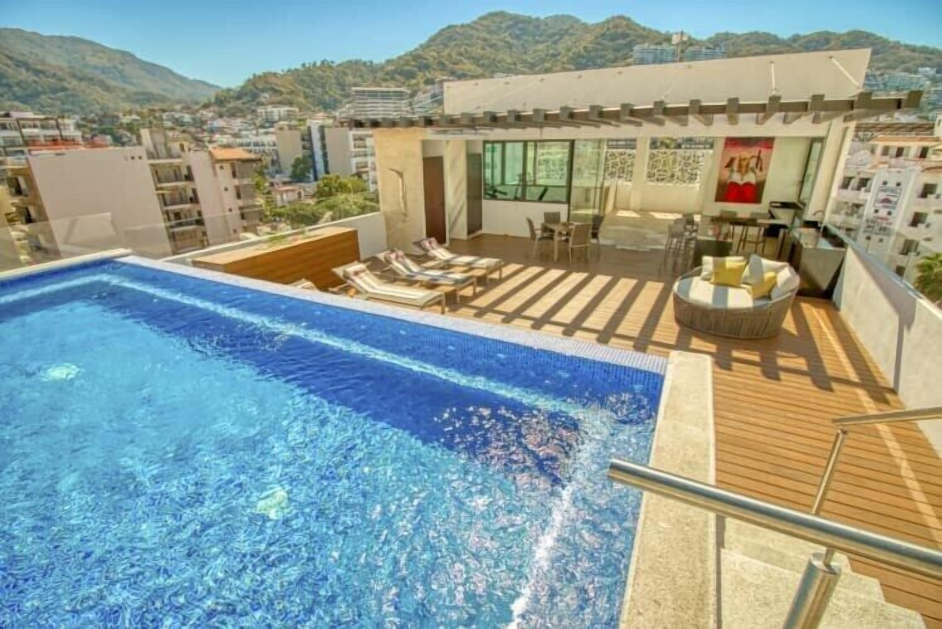 Un espace piscine aménagé sur le toit, avec des chaises longues et un bar.