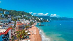 A coastal cityscape with a beach, buildings, and a bridge over the water. - Incredible new condo 1/2 Block from Beach/Malecon! (Puerto Vallarta)