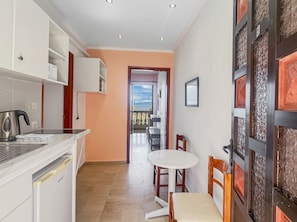 A kitchen with a kettle, a small table, and chairs, leading to a balcony with a view.