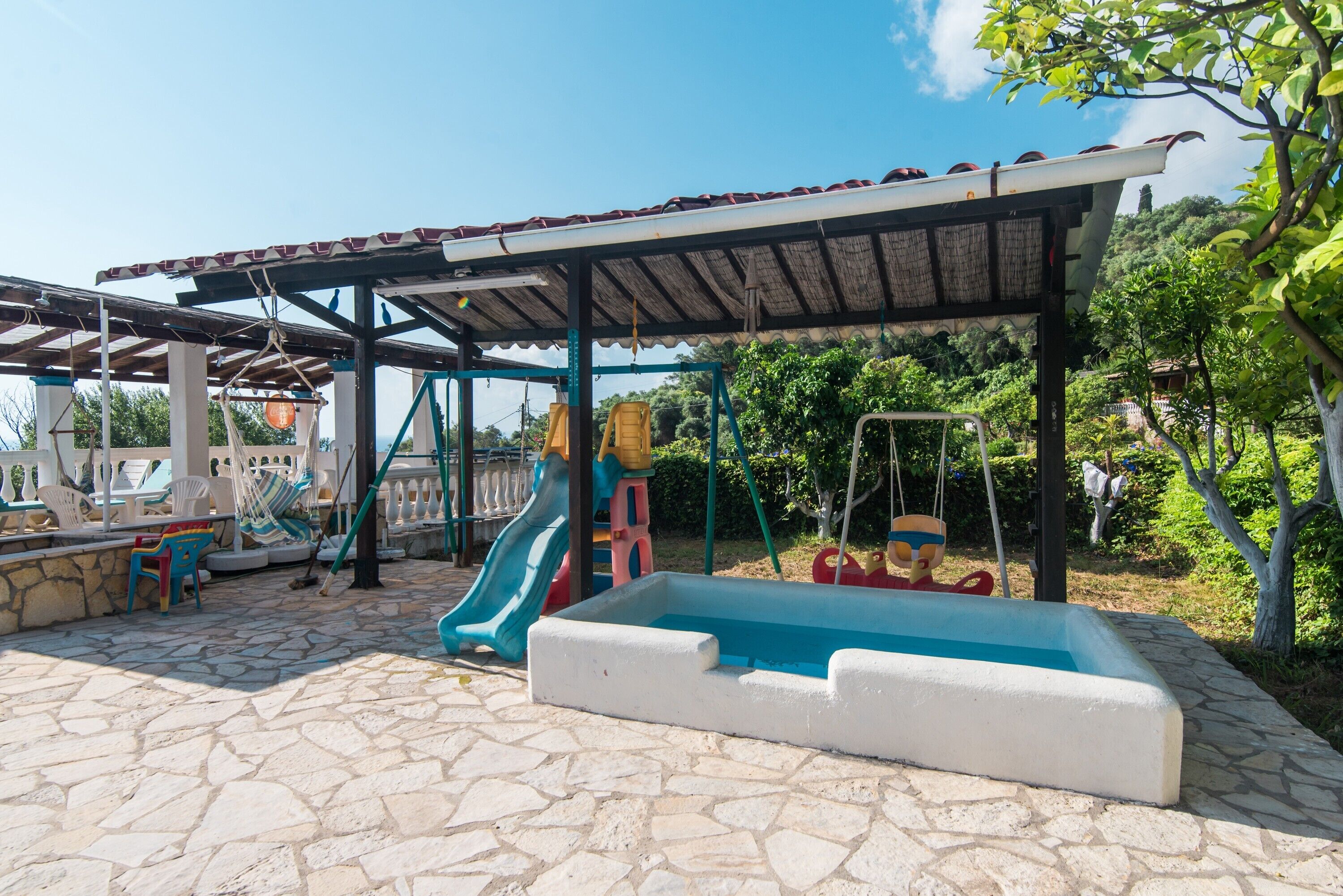 Un'area esterna riparata con piscina, strutture giochi e pavimento in pietra.