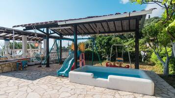Un'area esterna riparata con piscina, strutture giochi e pavimento in pietra.