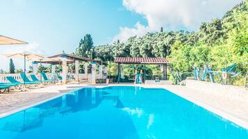 Una piscina con lettini, un gazebo e vista su un pendio boscoso.