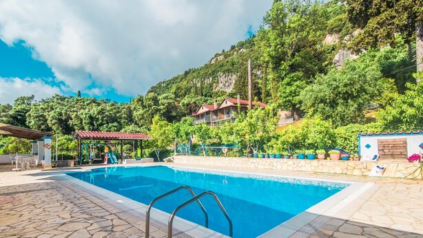 Une piscine dont le fond est recouvert de pierres, entourée de verdure et située au pied d’une colline.