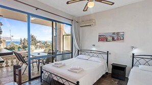 A bedroom with a bed, a ceiling fan, an air conditioning unit, a dining table with chairs, and a view of the sea. - Andromaches Large Apartment 2 with Sea View, Wi-Fi and Air Conditioning (Corfu)