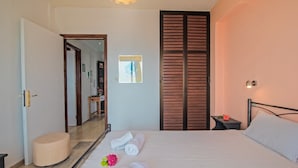 Hotelkamer met een bed, nachtkastje met een bloem, een spiegel, een houten kledingkast en een deur naar een andere kamer.