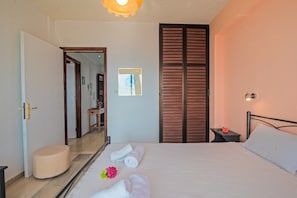 Une chambre d’hôtel avec un lit, une table de chevet ornée d’une fleur, un miroir, une armoire en bois et une porte donnant sur une autre pièce.