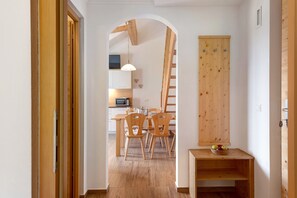 Ein Flur, der in einen Essbereich mit Holzsesseln und einem Tisch, einem Holzschrank und einem kleinen Regal mit Äpfeln führt.