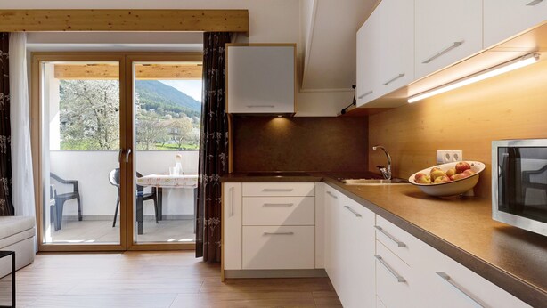 Une cuisine moderne avec des meubles blancs, un plan de travail en bois et un saladier rempli de fruits.