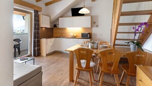 Une cuisine compacte avec des poutres en bois, un coin repas avec des chaises en bois, un réfrigérateur blanc et un four à micro-ondes.