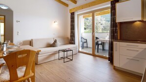 Un salon moderne avec un canapé, une table à manger et une petite table basse. Une porte-fenêtre coulissante donne accès à un espace extérieur aménagé avec une table et des chaises.