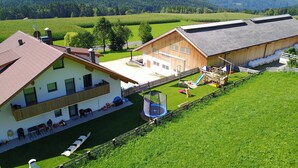 Une maison à deux étages avec un balcon, un espace de jeux doté d’un toboggan et une cour clôturée.