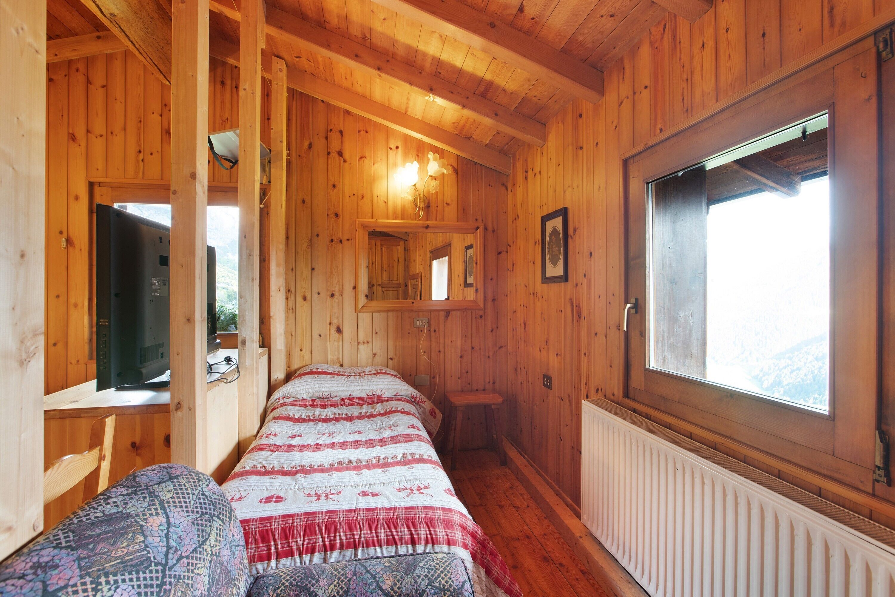 Una baita di legno con un letto, una scrivania, una finestra e un termosifone.