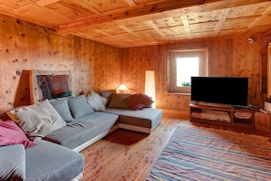 Interior de una cabaña de madera con sofá, televisión y ventana.