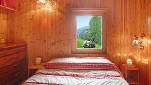 Ein Zimmer aus Holz mit einem Bett, einem Schminktisch und einem Fenster mit Blick auf grüne Vegetation.