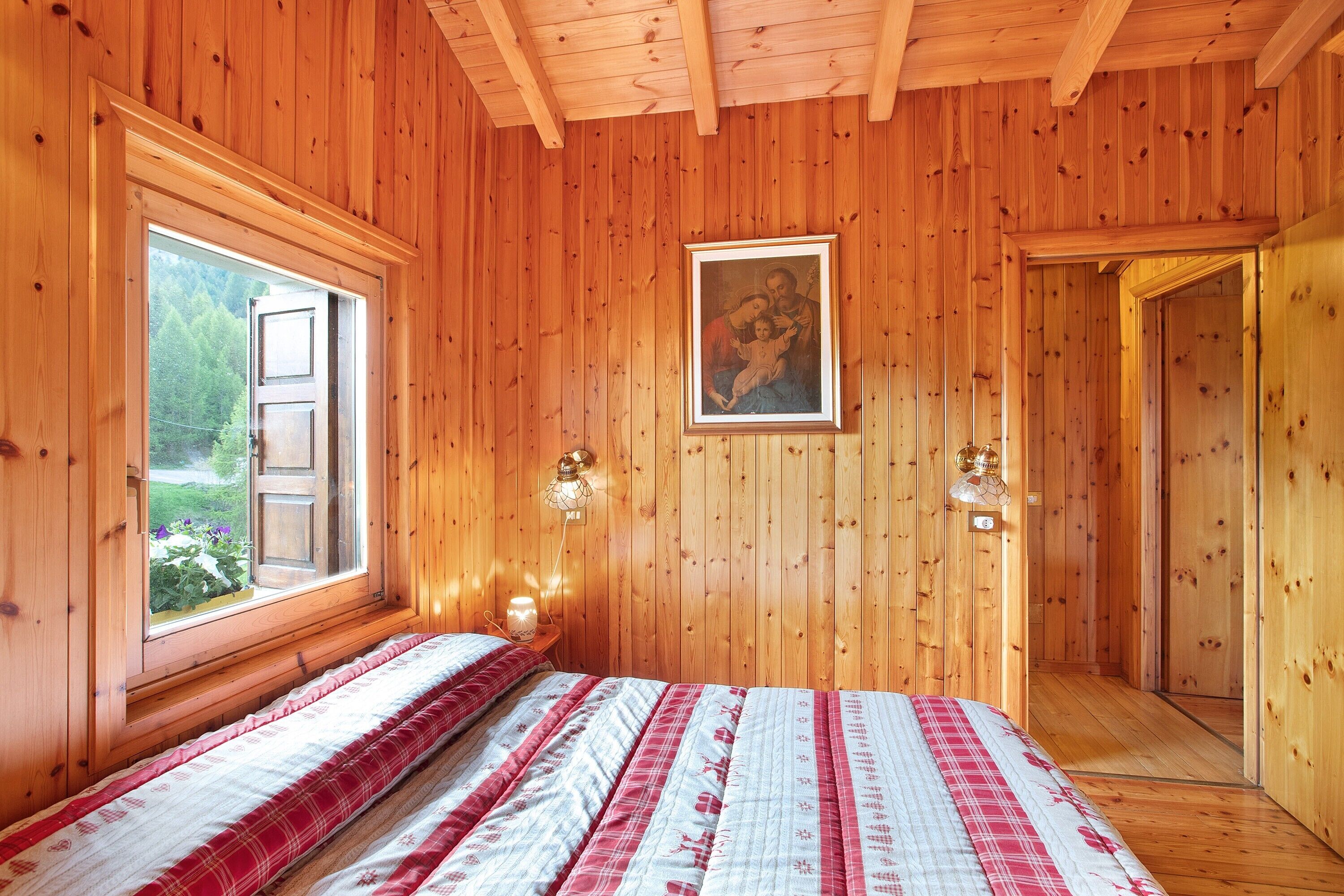 A wooden-paneled room with a bed, a window, a painting, and a door.
