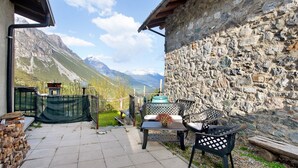 Eine Terrasse mit Gartenmöbeln, einer Steinmauer und Blick auf Berge.