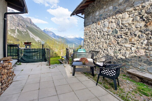 Un patio con mobiliario exterior, un muro de piedra y vistas a montañas.