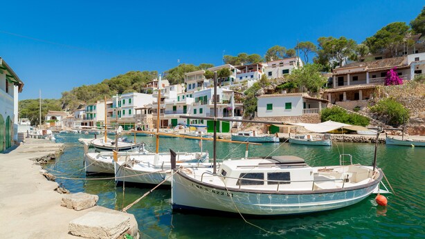 A coastal village with boats docked at a pier, traditional buildings, and a clear blue sky.