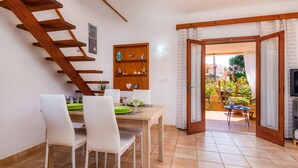 A dining area with a wooden staircase, a wooden shelf with decorative items, and a view of the outdoor garden through an open door.