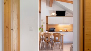 Eine moderne Küche mit weißen Schränken, einem Esstisch mit Holzstühlen und einem Fernseher über der Arbeitsfläche.