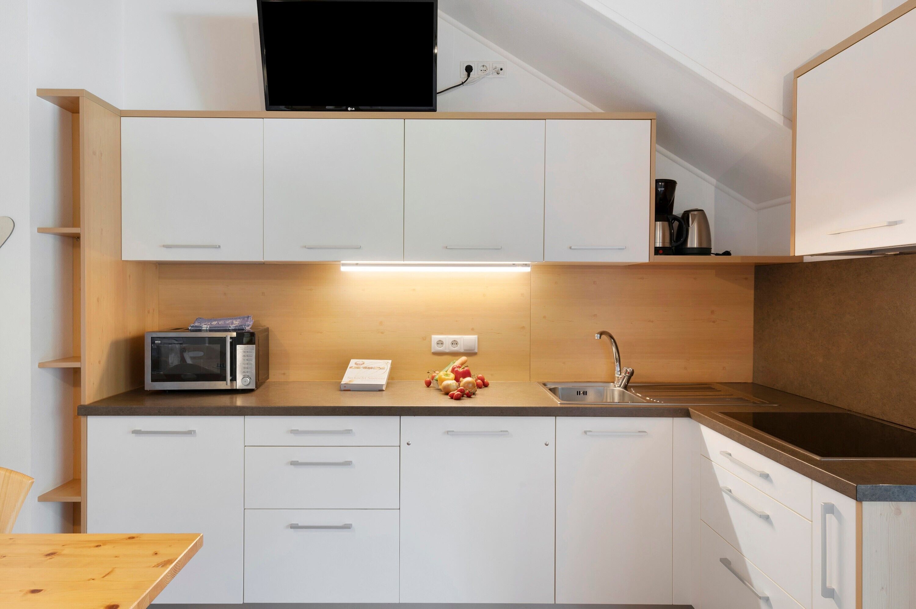 Una cocina moderna con armarios blancos, microondas, cafetera y pileta.