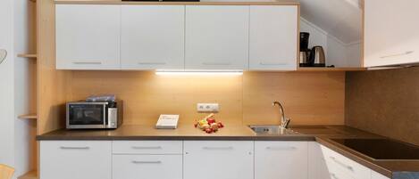 Una cocina moderna con armarios blancos, microondas, cafetera y pileta.