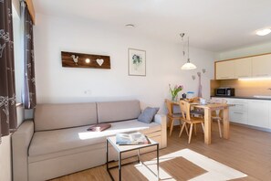A modern living space with a sofa, a dining table with chairs, a kitchen area, and artwork on the walls.