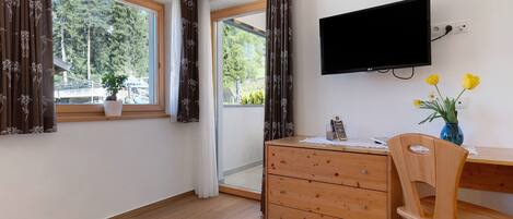 A room with a wooden desk, a chair, a TV mounted on the wall, and a window with curtains.