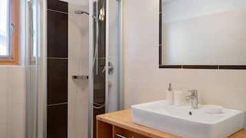 Ein modernes Badezimmer mit einer gläsernen Duschkabine, einem weißen Waschbecken mit zwei Tassen und einem Spiegel darüber.