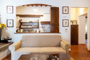 Een woonkamer met een bank, een salontafel, en een keukenhoek met planken en kastjes.