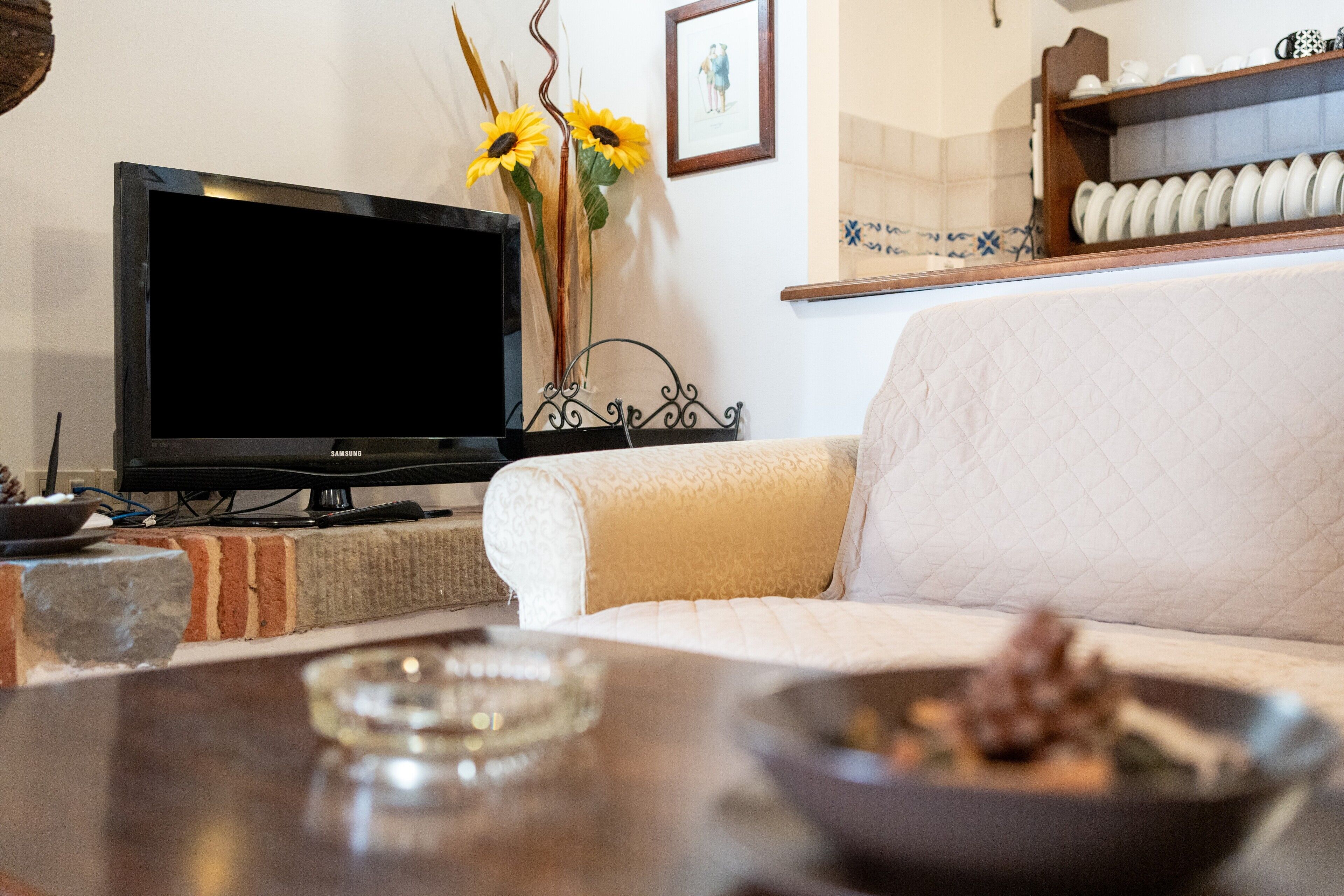 Een woonkamer met een televisie, bank en een decoratieve vaas met zonnebloemen.