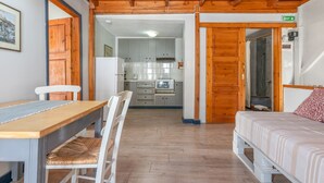 Ein Zimmer mit Holzboden, einem Bett mit gemustertem Bettbezug, einem Esstisch mit Stühlen und einer kleinen Küche im Hintergrund.