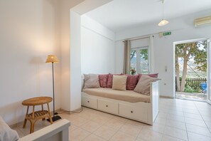 A room with a sofa, a lamp, a small stool, and a view of the outdoors.
