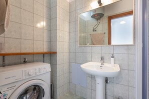 Un bagno compatto con lavatrice, lavandino e specchio.
