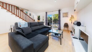 Un salon moderne avec un canapé, une table basse et un téléviseur. Un escalier en bois mène à un autre niveau.