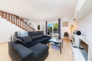 Ein modernes Wohnzimmer mit einer Couch, einem Couchtisch und einem Fernseher. Eine Treppe mit Holzwangen führt zu einer weiteren Ebene.