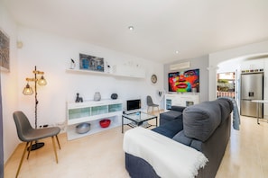 Ein modernes Wohnzimmer mit Sofa, Fernseher und einem Essbereich mit Kühlschrank.