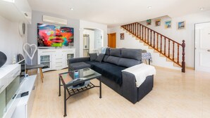 Un salon avec un canapé, une table basse, un téléviseur et un escalier.