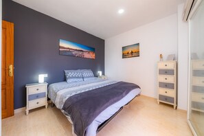 Une chambre à coucher comprenant un lit, des tables de chevet, une commode, une coiffeuse et deux tableaux accrochés au mur.