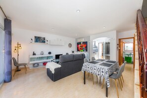 Un salon moderne avec un canapé gris, une table à manger et des chaises, une console blanche et un téléviseur.