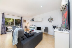Ein modernes Wohnzimmer mit Sofa, Fernseher und einem Balkon mit Vorhängen.